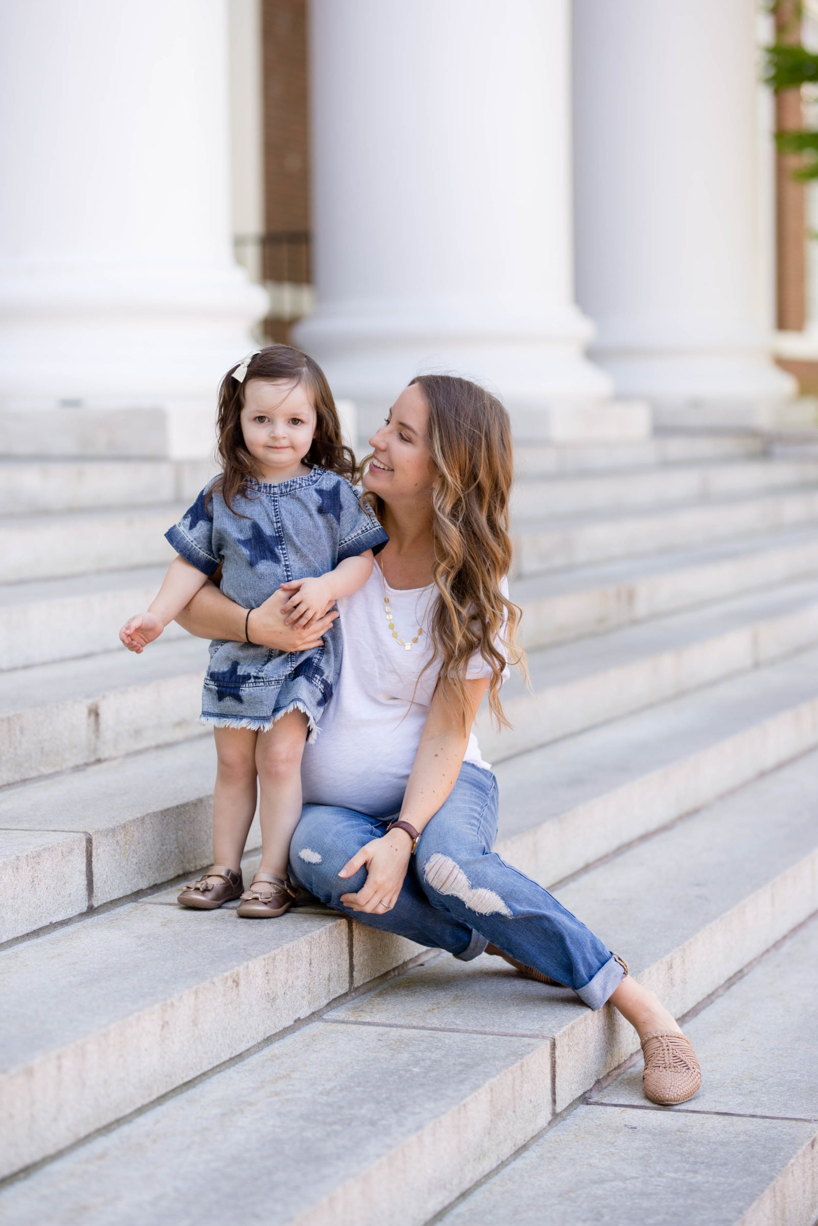 Mom sitting on stone steps holding her toddler daughter in a denim star dress