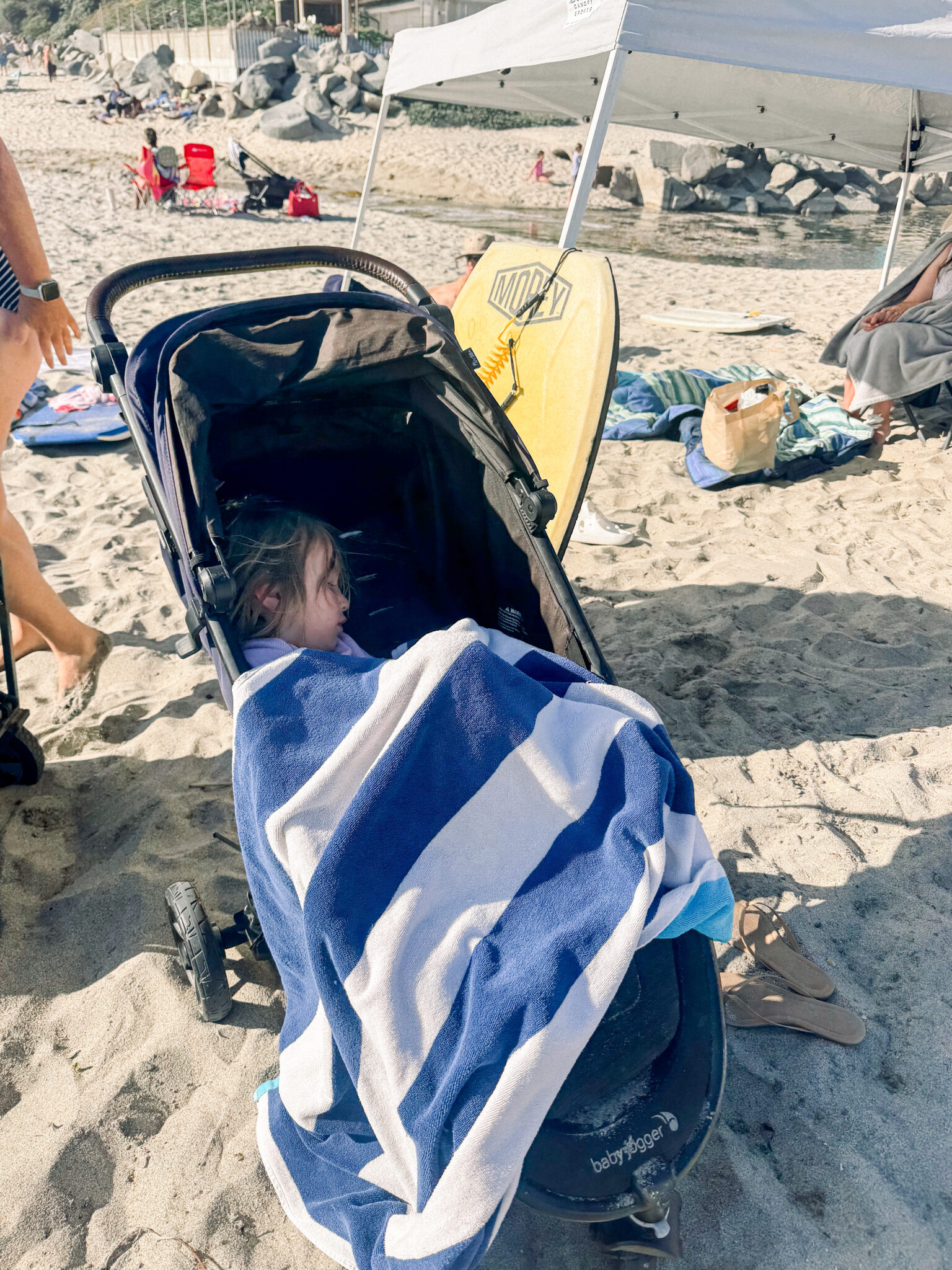 baby asleep in a travel stroller at the beach.