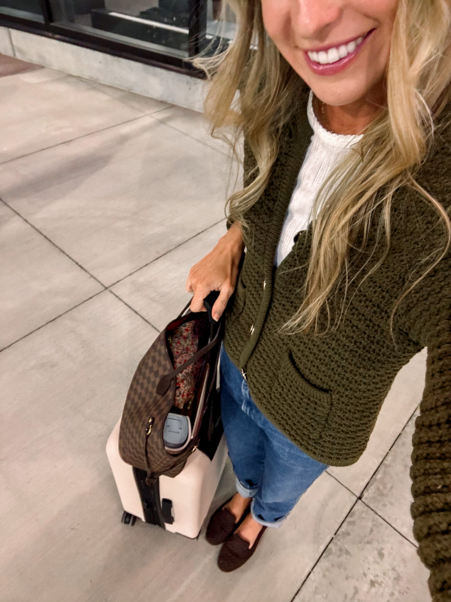 A woman standing at the airport after flying allegiant with her carryon suitcase.