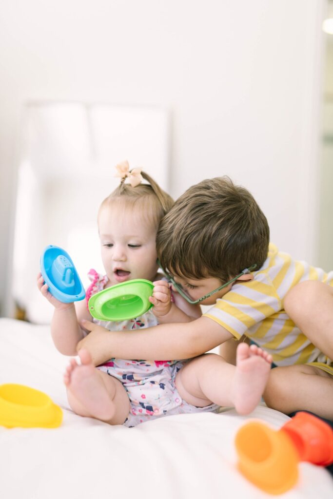 Big brother hugging his baby sister as she plays with stacking boats